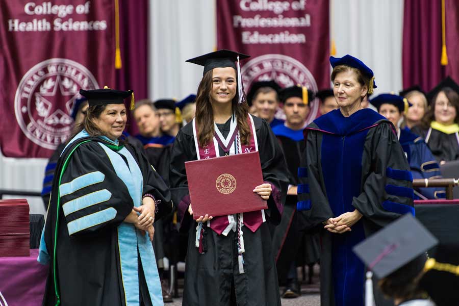 A TWU student stands on stage during commencement after receiving her honors medal.