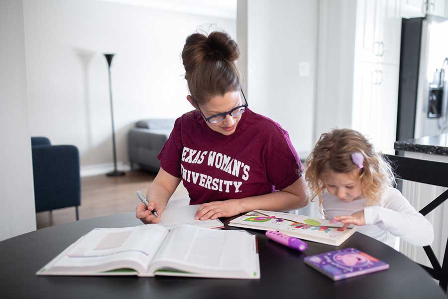 A TWU student studies at home with her daughter next to her at the table.