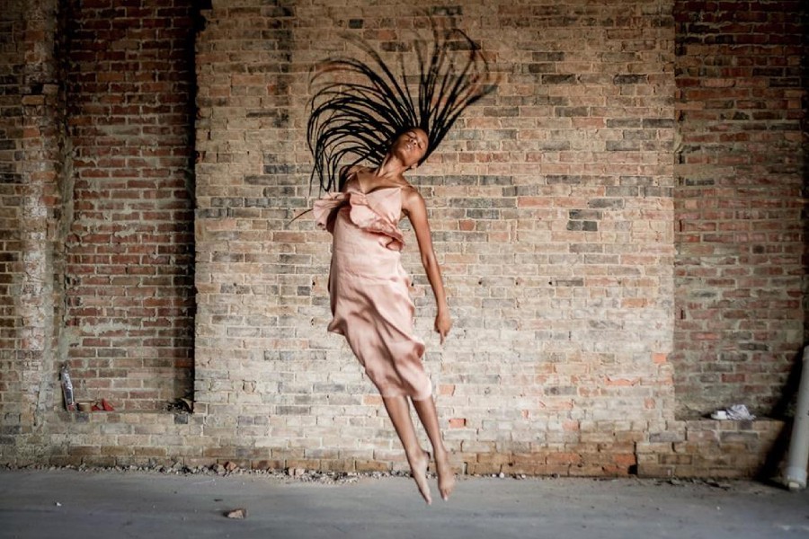 Asiyah Martin dancing with a scenic brick wall behind her.