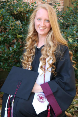 Audra Romans smiling and posing outdoors in her graduation cap and gown.