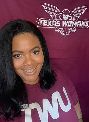 Chanel VanHook dressed in TWU maroon with the athletics barn owl logo in the background.