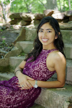 A portrait of Jassmine Marquez sitting outdoors on the steps of a garden.