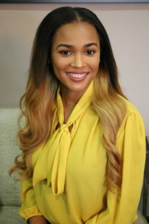 A portrait of Deyaun Seale smiling and posing sitting down in a yellow blouse.	