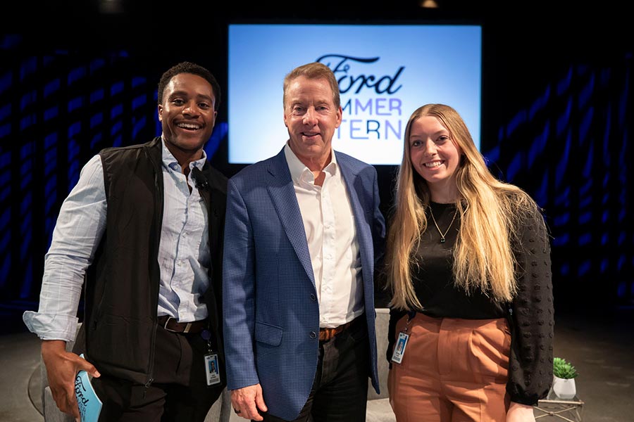 two summer interns stand on either side of an executive in front of a screen that says Ford