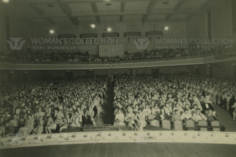 An audience in Margo Jones Hall in the 1920s. Several members of the audience appear to be in costume. A 13-star American flag hangs from the right side balcony.