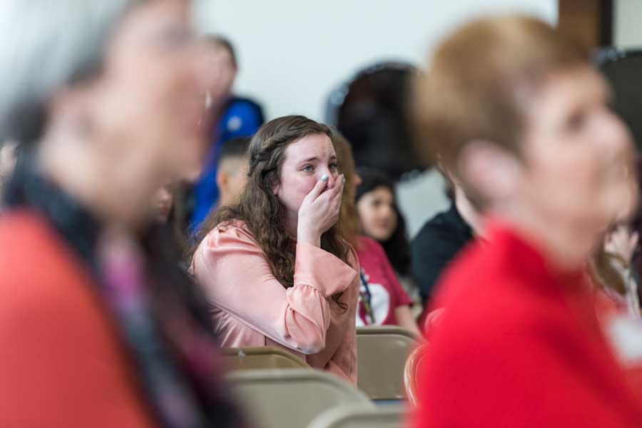 Caroline Deitch makes a surprised expression in a crowd in her high school auditorium.