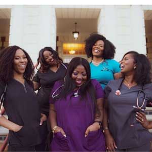 Five women in scrubs smile outside.