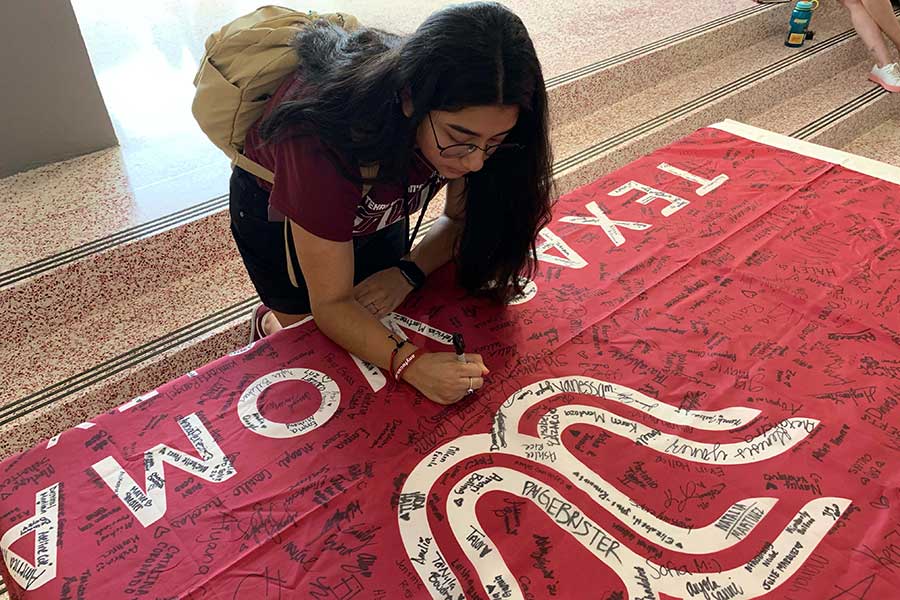 A TWU student signs a maroon flag with the TWU logo on it.