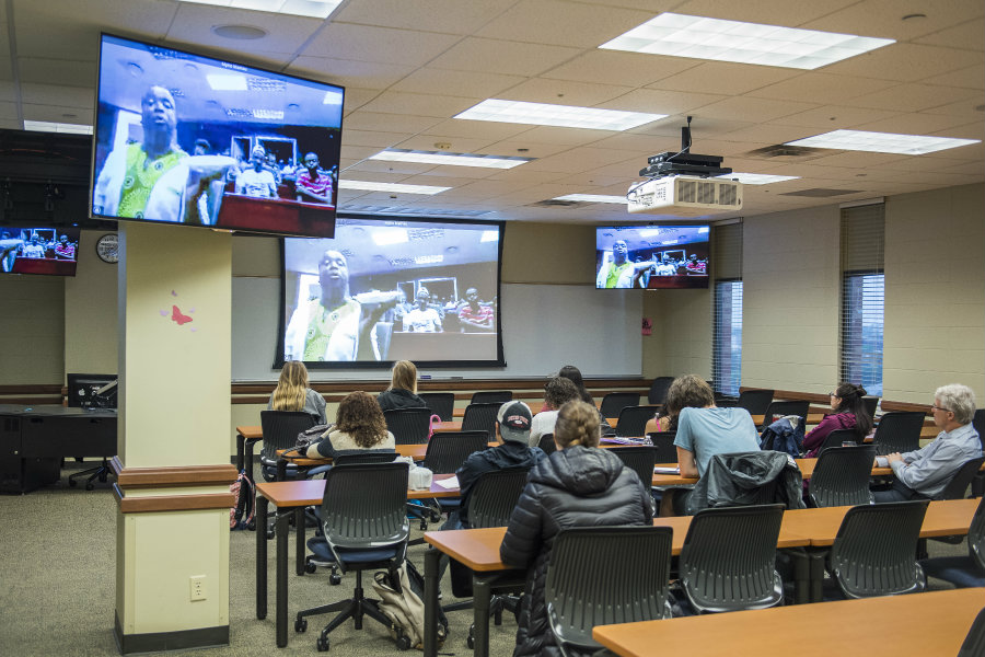 A classroom of students watching as South African students on the TV screen show them a traditional meal.