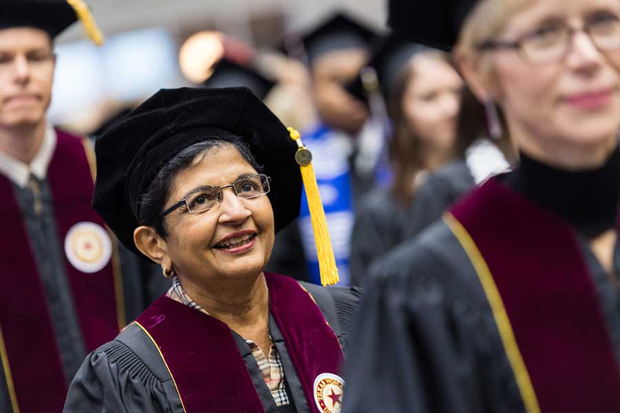 Kiran Kanwar walks in doctoral academic regalia during her commencement ceremony at TWU.