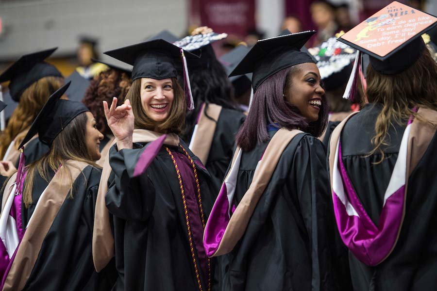 Smiling graduates, with one woman flashing "I love you" hand sign.
