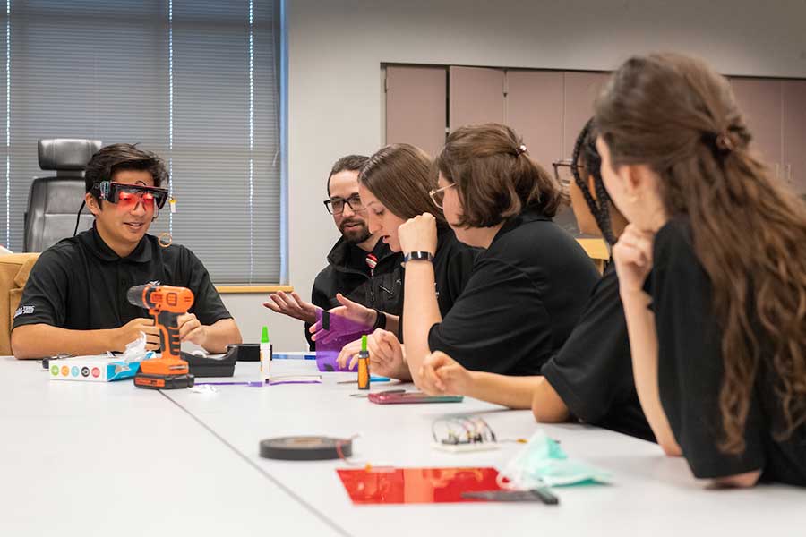 TWU students around a table working on an electronic device.