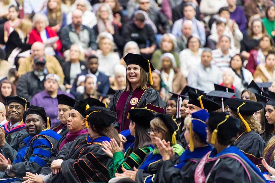 Nicole Carroll stands in doctoral academic regalia during her commencement ceremony.