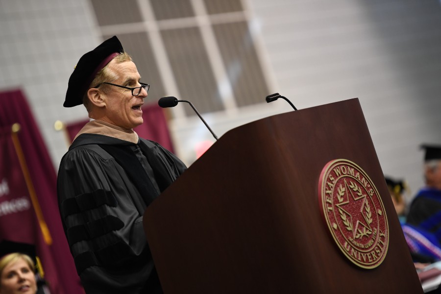 Robert S. Kaplan speaking on stage at a podium in academic regalia.	