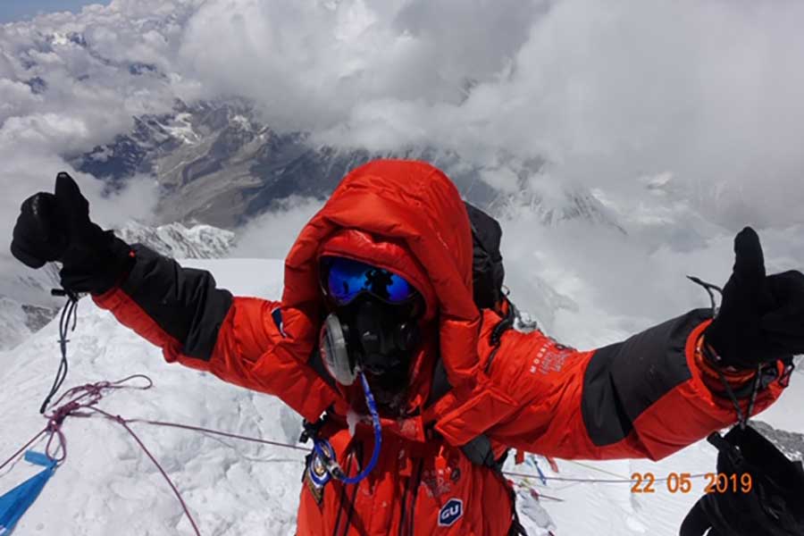 climber in red jacket stands atop of mountain