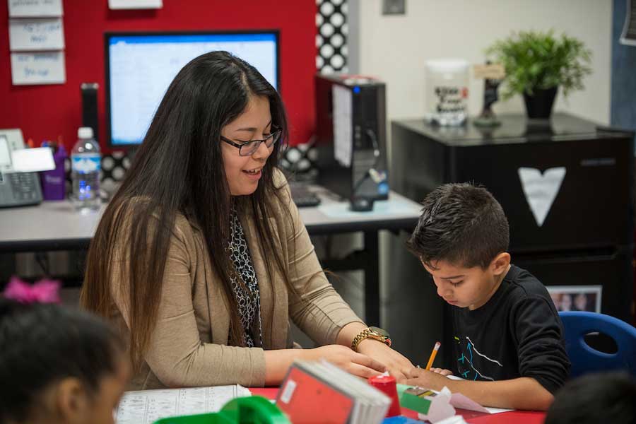 A hispanic TWU student teaches a young boy in a classroom setting.
