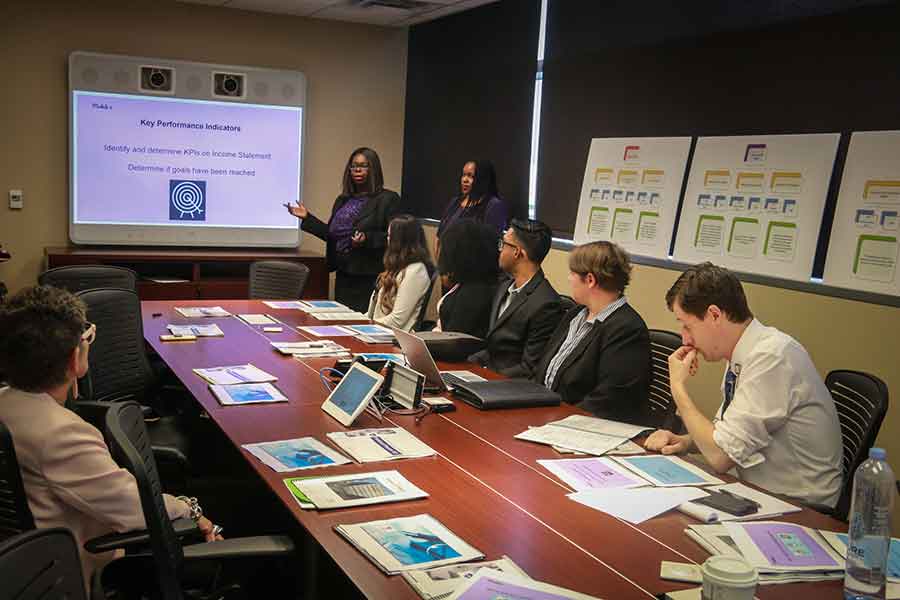 Three TWU students give a presentation in a board room filled with professors and hospital executives.