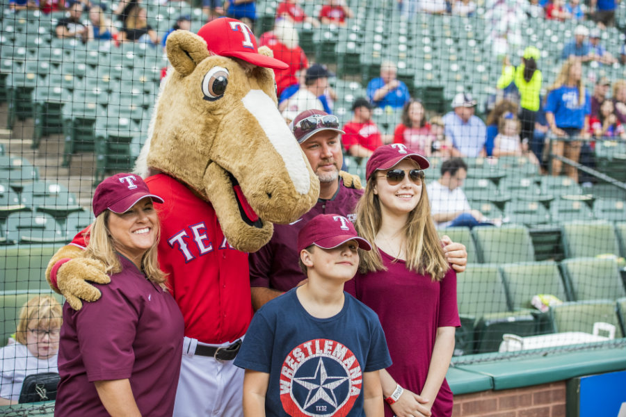 TWU Softball coach posing with her family and the Texas Ranger's mascot, Captain.	