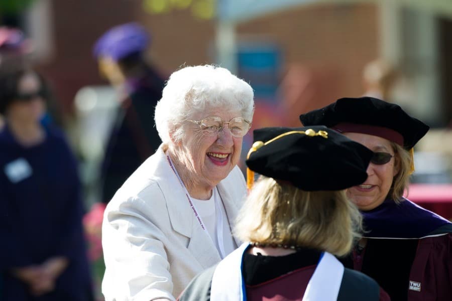 Bettye Myers smiling outdoors with two doctoral graduates at commencement.