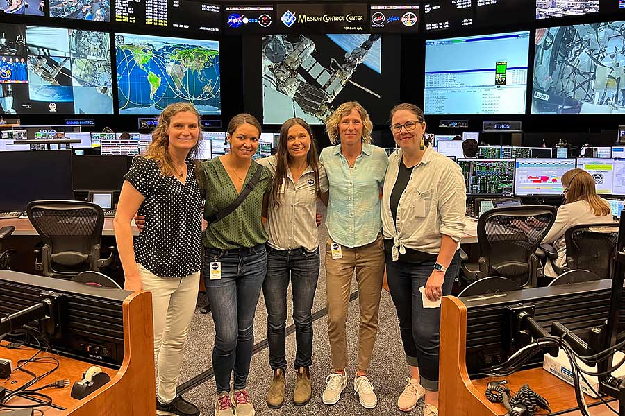 five women stand in front of numerous tv monitors