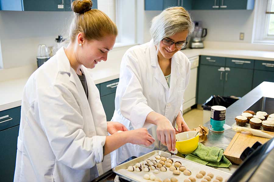 Two TWU students cook in an industrial kitchen setting.