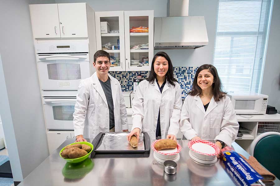 Three TWU students prep to begin cooking in an industrial kitchen setting.