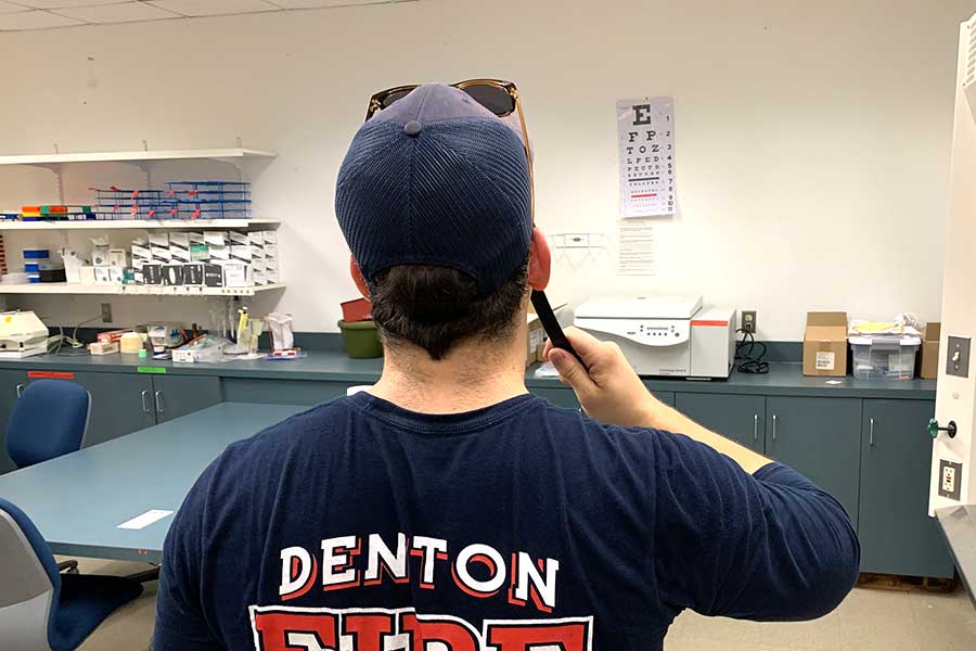 firefighter, from behind, holding up eye stick in exam room 