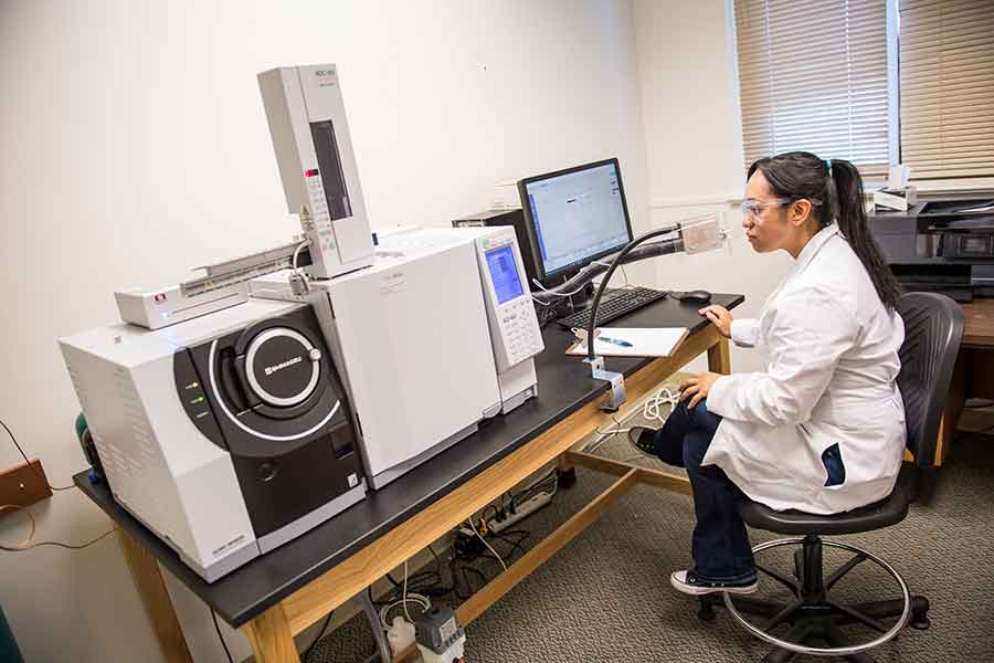 A TWU student works in a lab with a flavor chemistry research instrument.	