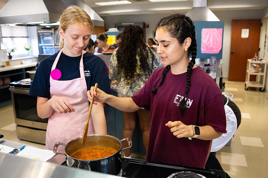 TWU student Mariana Salazar stirs a pot on stove next to a camper