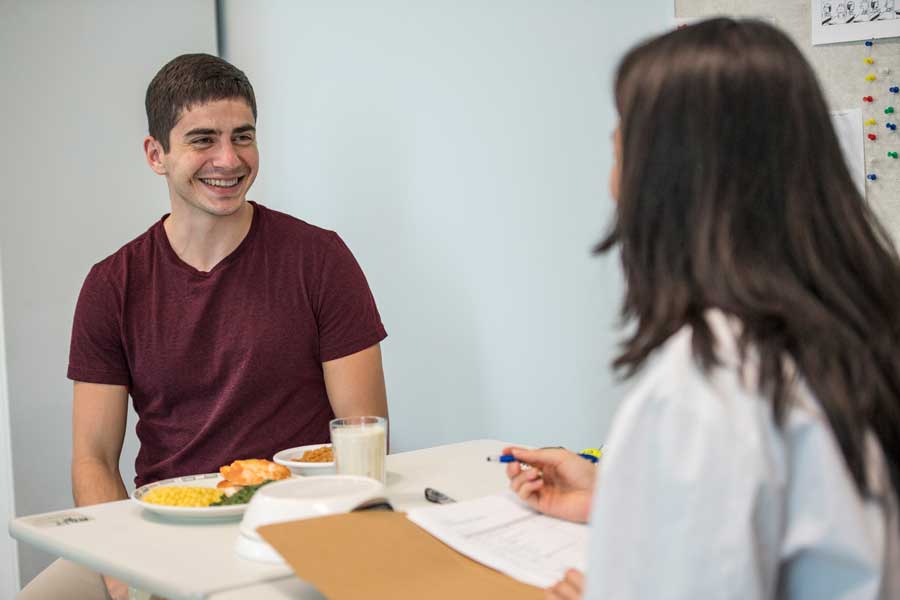 Female TWU dietitian talks to a male patient who has food options on table in front of him.