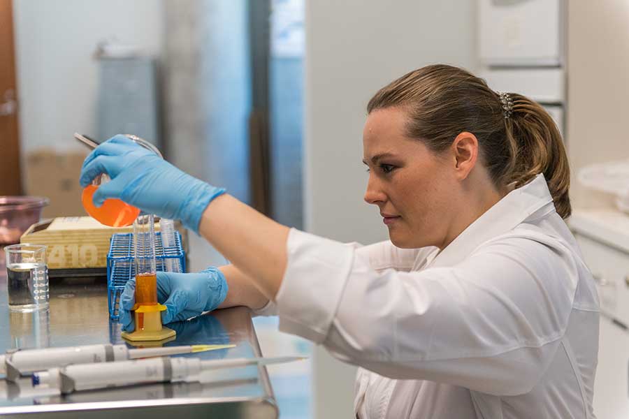 A young woman working on research in a lab setting and wearing safety gear.