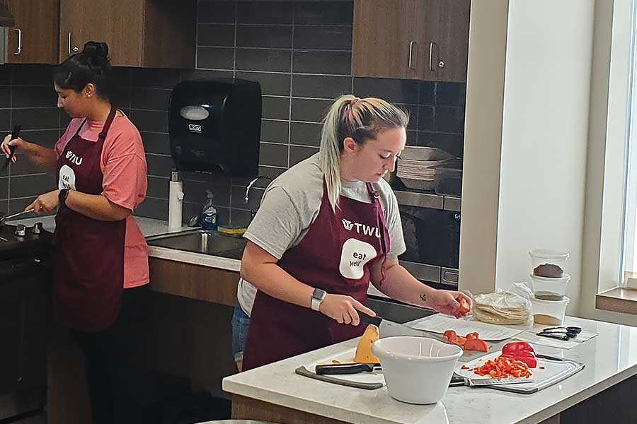 two students in aprons prepare food in kitchen 