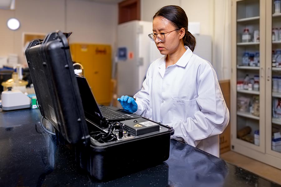 Danhui Wang stands behind a Raman spectroscopy