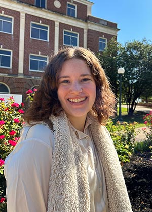TWU student Abby Schiwitz in front of a school building and flowers