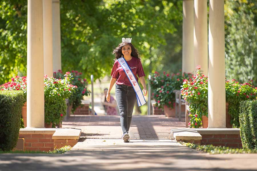 Aryana Bosh wearing the Miss Black Texas crown and sash walks between pillars