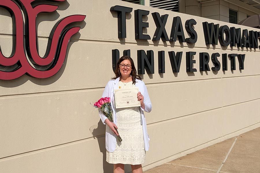 Jessica Marchant stands next to the TWU logo on the Houston campus
