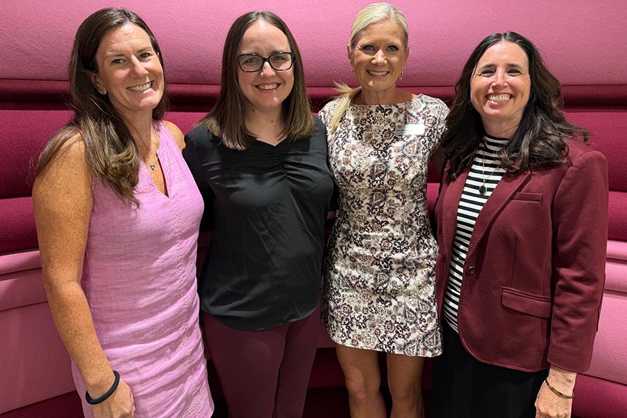 four TWU faculty members stand in front of a pink and maroon background