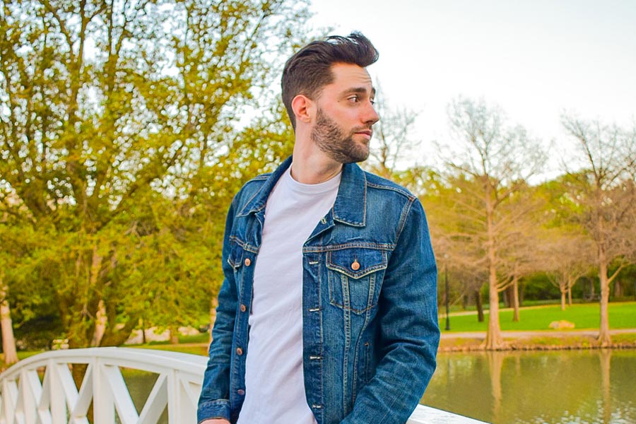 a TWU student wearing a jean jacket poses on a bridge with trees in the background
