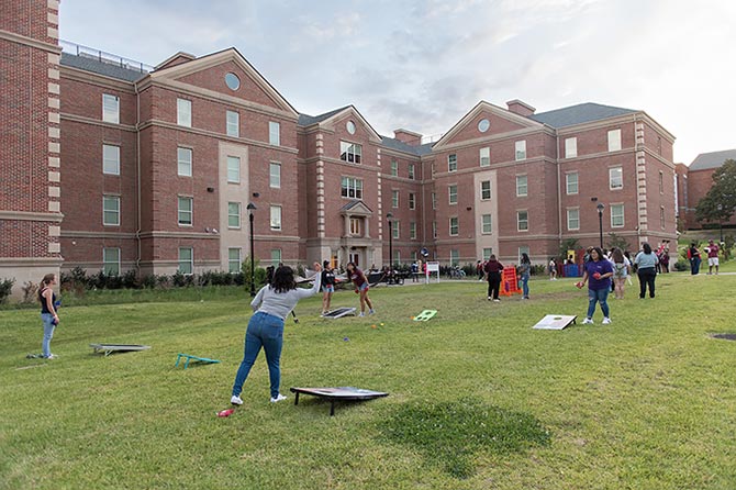 A group of TWU students play bean bag toss on the lawn of the Parliament Village dorms
