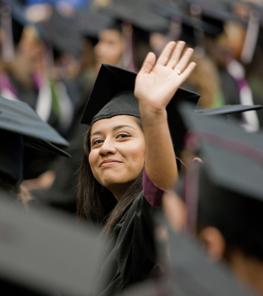 Student in cap and gown waving to family.