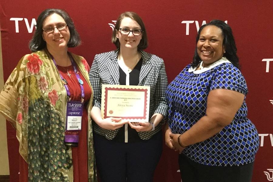 Three women, smiling. Woman in center holds certificate.