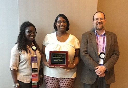 Two African-American women and a white male pose with award