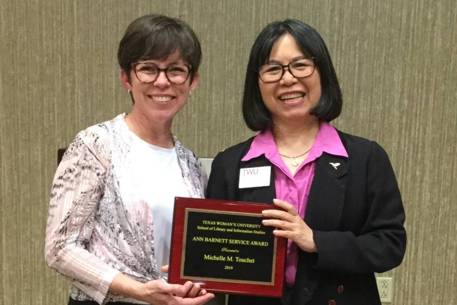 Two women standing, holding plaque.