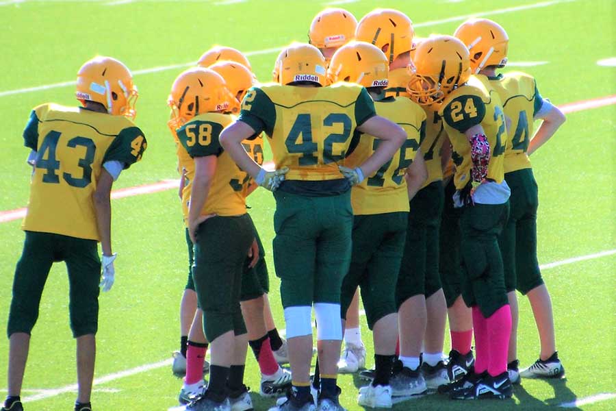 middle school football players in a huddle, wearing yellow uniform and helmets with green pants
