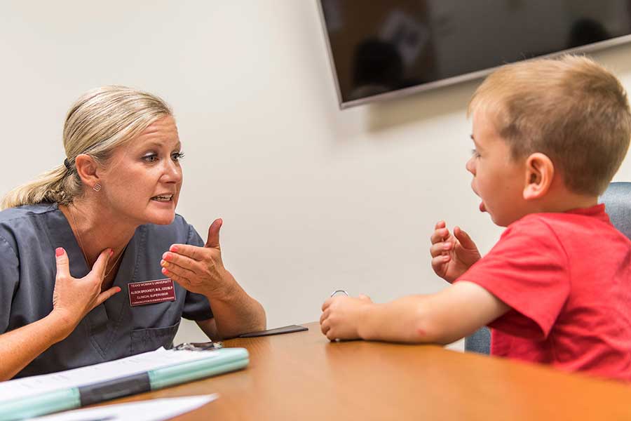 Speech Clinic Director Alison Brockett makes a gesture with her hand to a young boy sitting across from her at a table