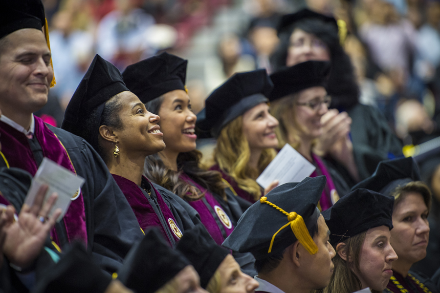 Graduate students wearing tams caps with tassels smile at the commencement audience.