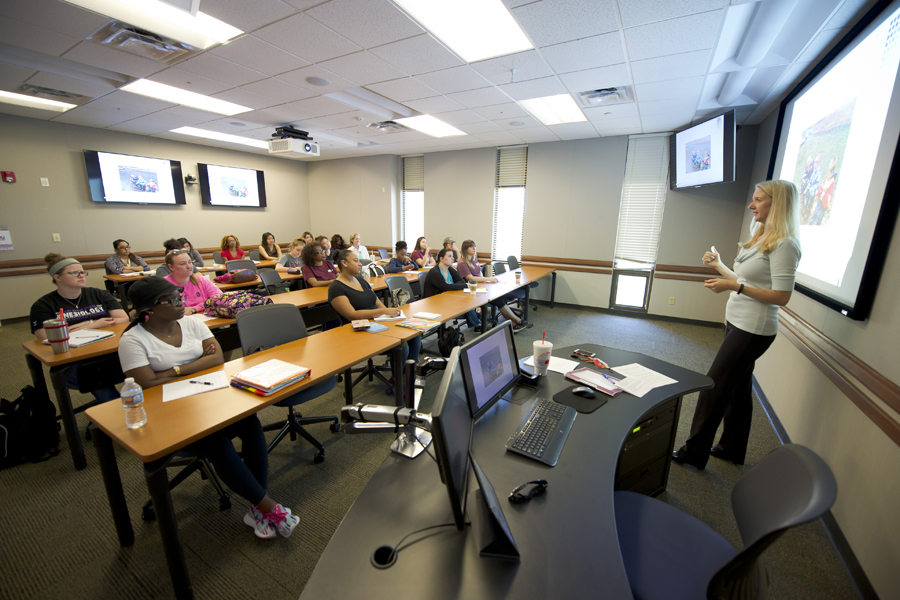 professor stands in front of a white screen in a classroom 