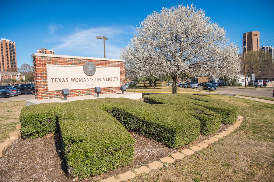 Topiary shaped to form the letters 'TWU', located in front of the Texas Woman's University sign on Bell Ave. 