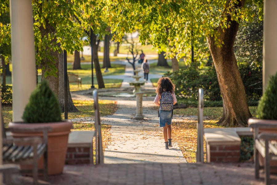 A TWU student walks through fall foliage near the Gertrude Lathrop Arbor.	