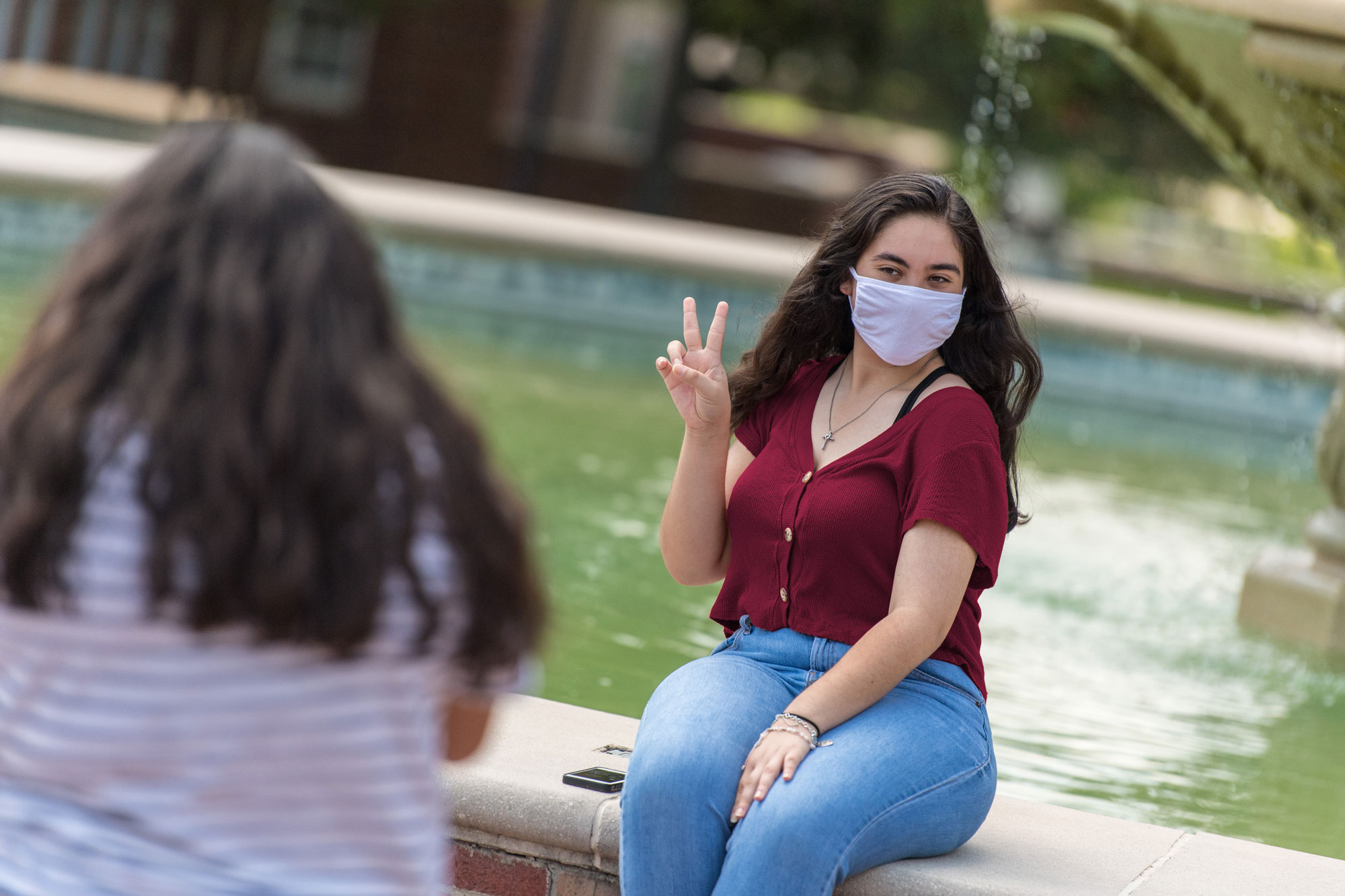 A TWU student wearing a face covering poses at the Denton campus fountain.	